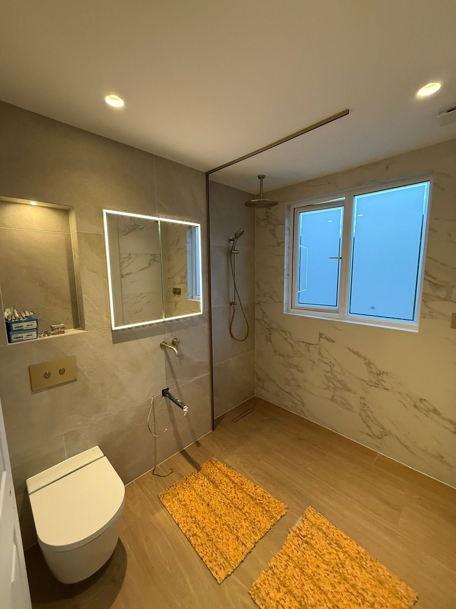 Finished bathroom with a walk-in shower, wall-hung toilet, illuminated mirror, recessed niche and marble-effect tiles