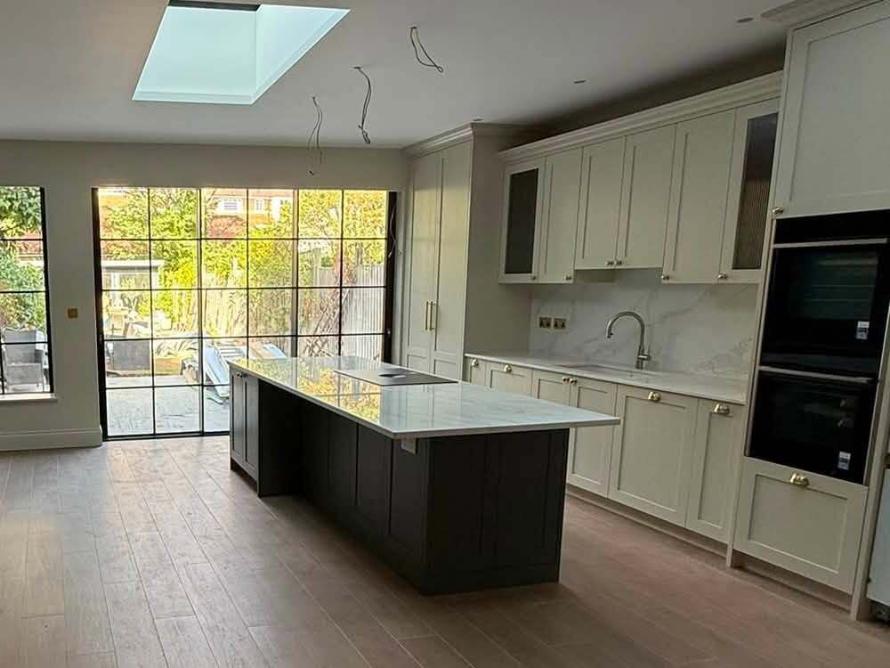 Shaker-style kitchen with a dark island, stone worktops, built-in ovens and a roof light over the island